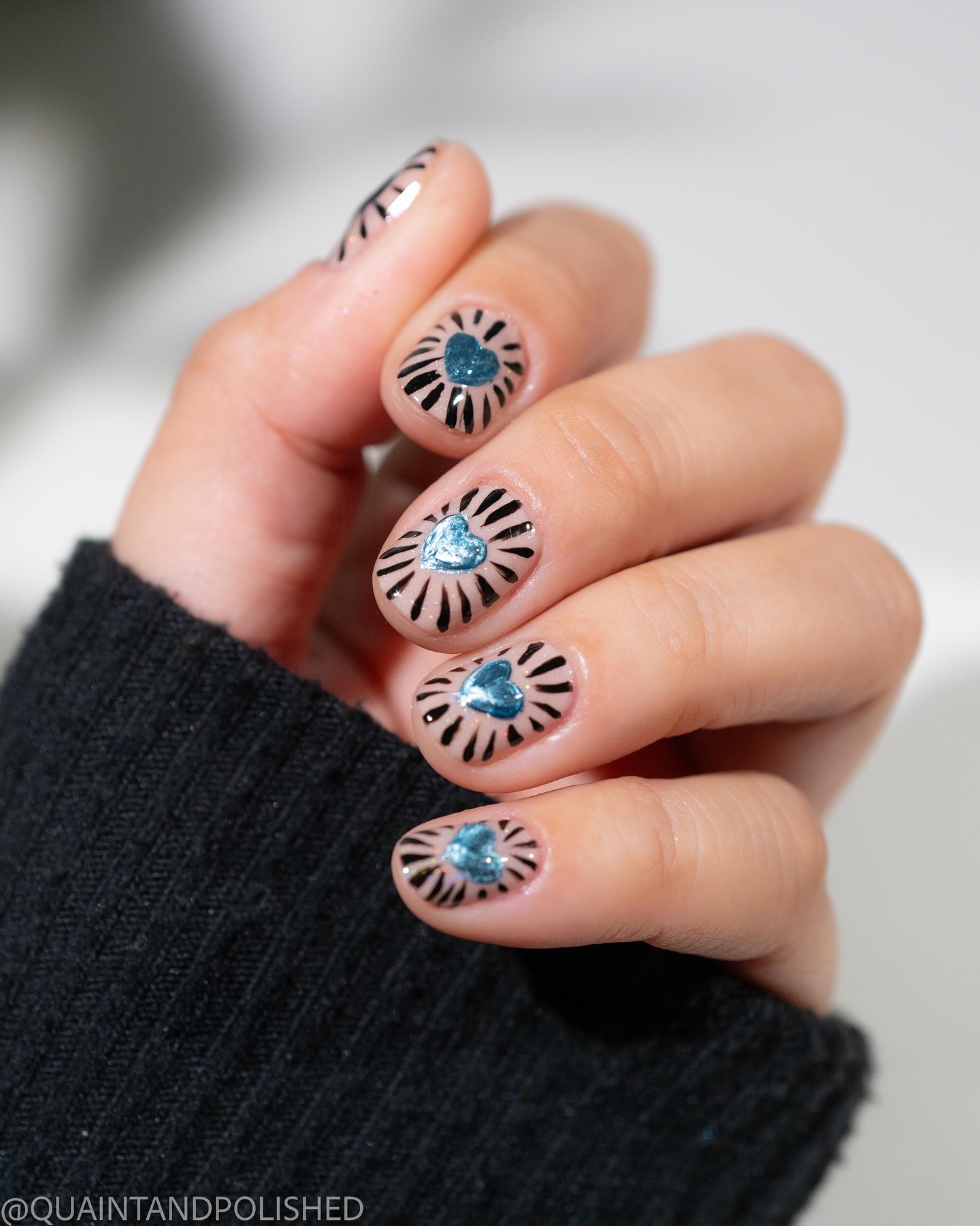Black lines radiate from a blue heart on nude nails.